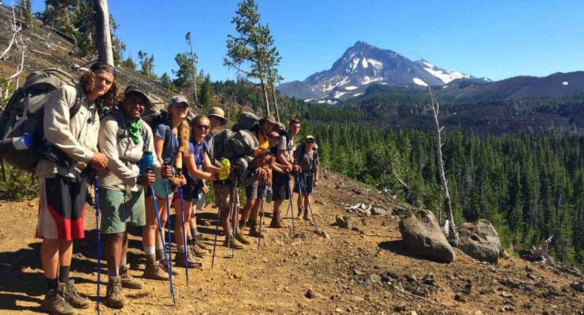 a group of teens pose with a mountain on backpacking trip